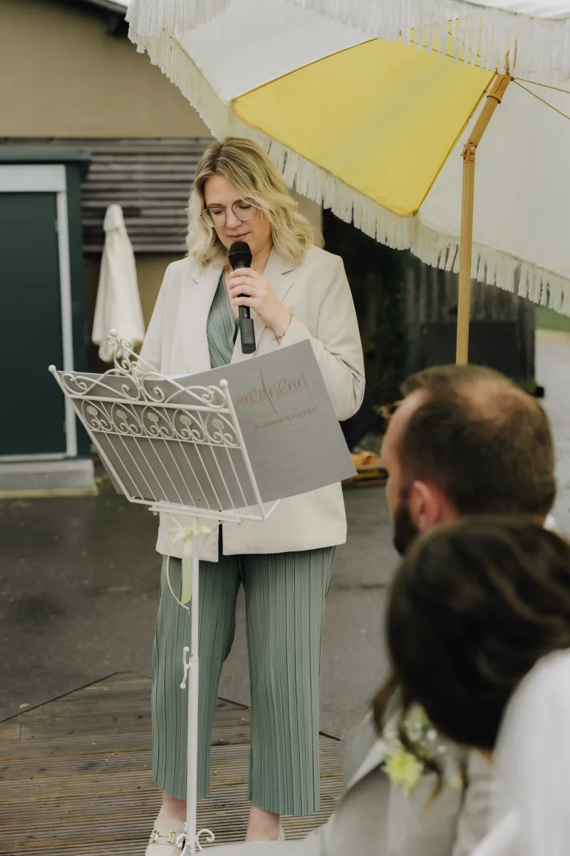 Traurednerin Yvonne Krienke hält die Traurede am Notenständer unter einem Sonnenschirm
