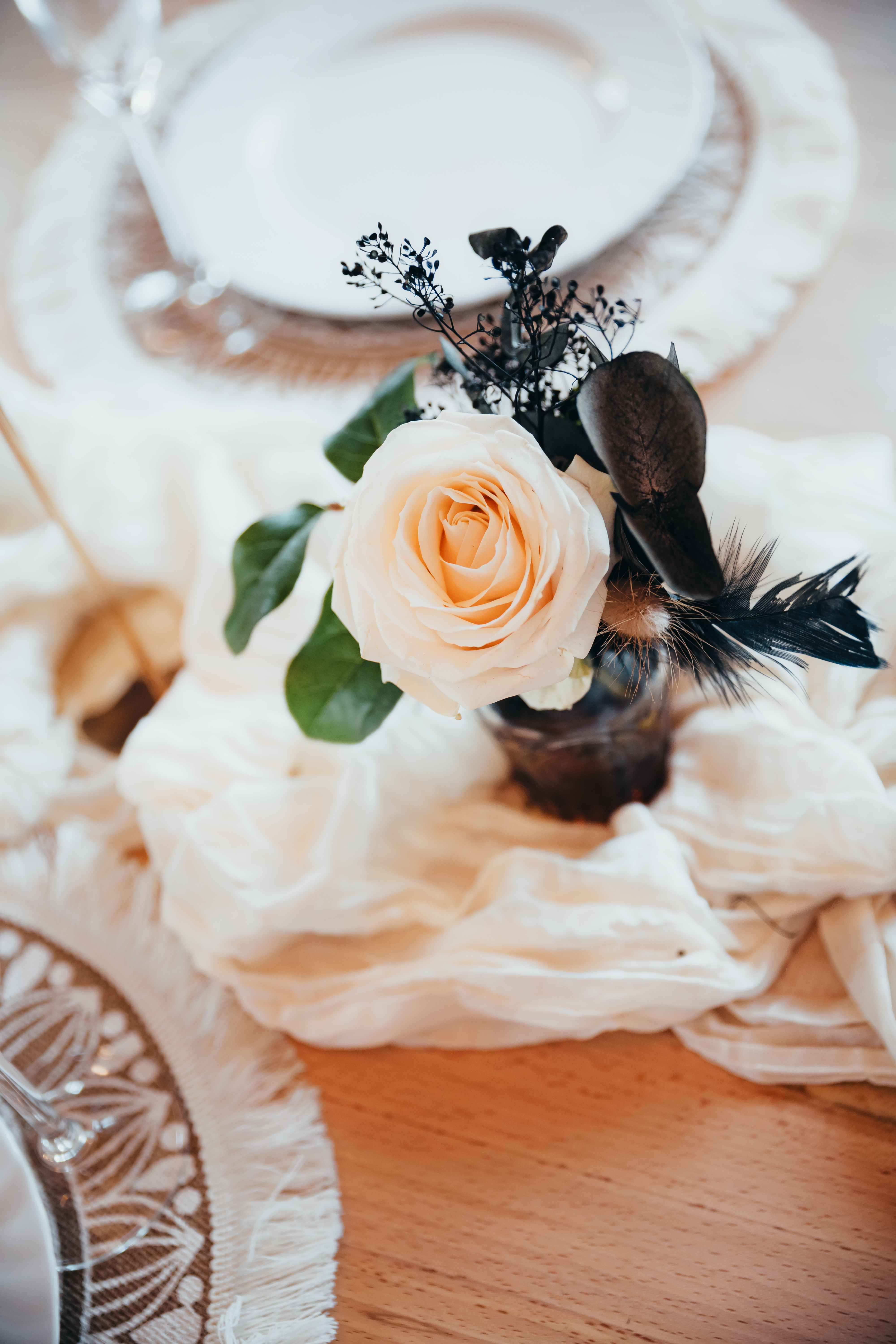 Zartrosa Rose mit dunklen Federn auf Hochzeitstisch – Cloud Dancer Ton