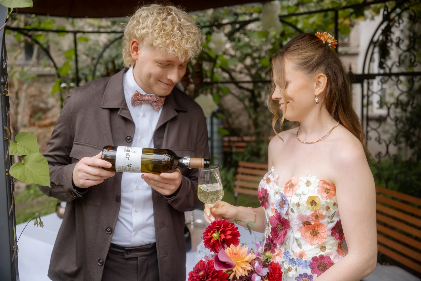 Bräutigam schenkt seiner Braut unter einer bewachsenen Pergola Sekt ein