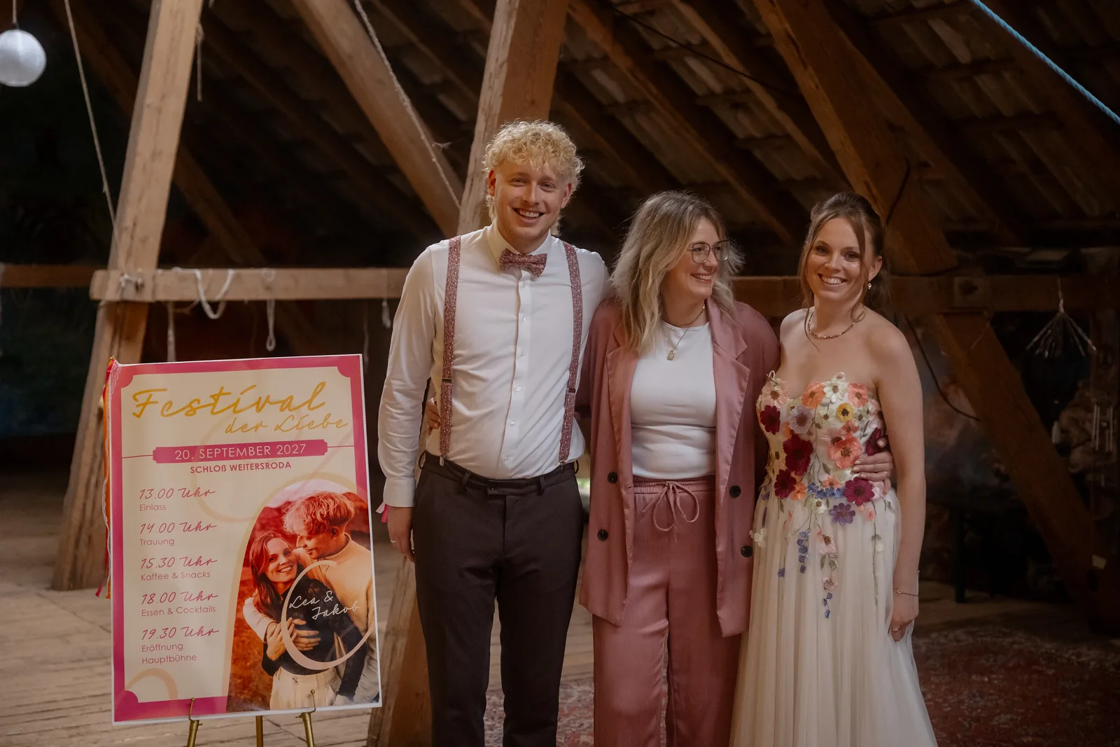 Weddingdaymanagerin Yvonne Krienke mit dem Brautpaar auf dem Dachboden von Schloss Weitersroda, daneben das Plakat mit dem Ablauf des Tages