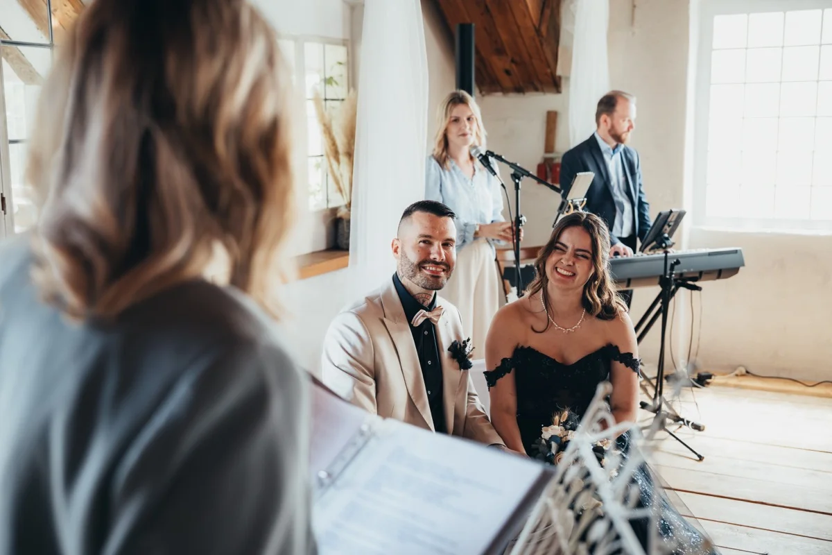 Lachendes Brautpaar während der freien Trauung, im Hintergrund Live-Musik
