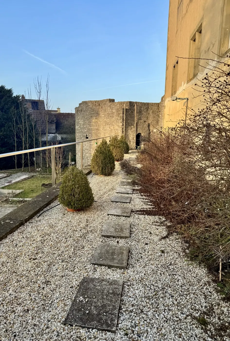 Kiesweg mit Trittplatten entlang der Burgmauer von Burg Arnstein, dahinter der alte Wehrturm mit Durchgang