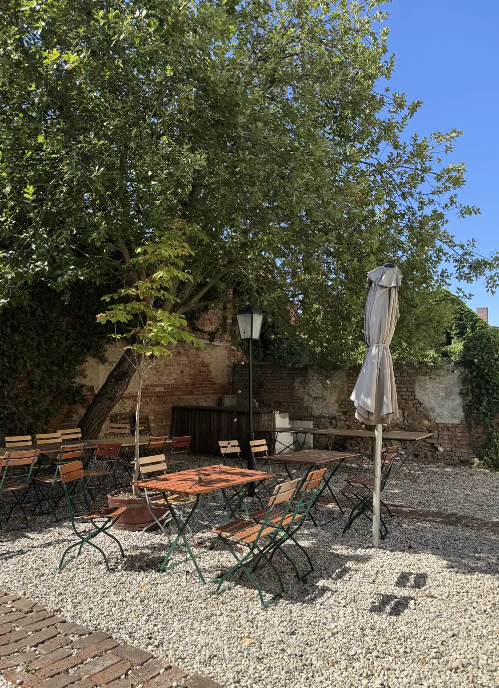 Biergarten des Hotel Kastanienbaum in Herzogenaurach mit alter Ziegelmauer, großem Baum, Biergartentischen und Sonnenschirm auf hellem Kies