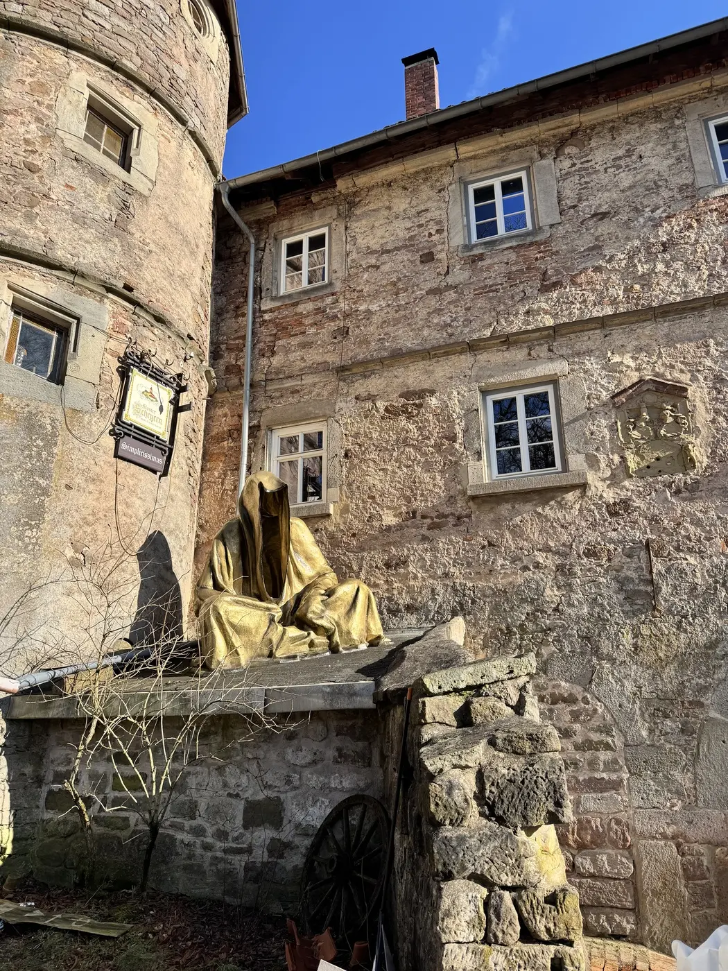 Runder Turm und alte Bruchsteinmauern von Schloss Weitersroda, auf einem Mauervorsprung sitzt eine goldene Kapuzenfigur