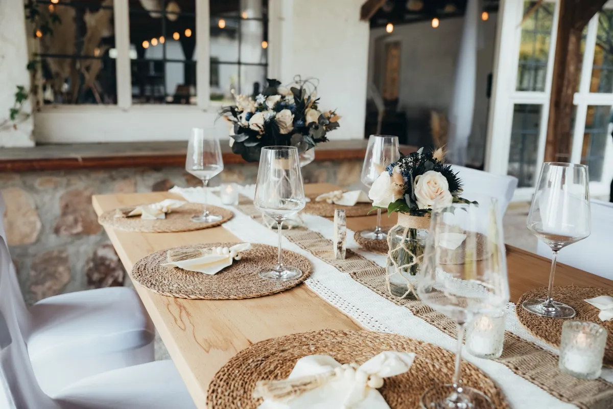 Gedeckte Holztafel mit Jute-Platzsets, Gläsern und Blumen